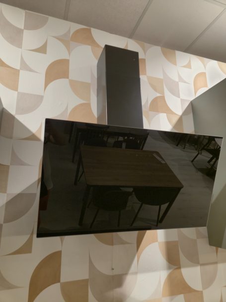 Moderne matgroene keuken Zwart scherm aan de muur boven een tafel met stoelen in een lichte ruimte.