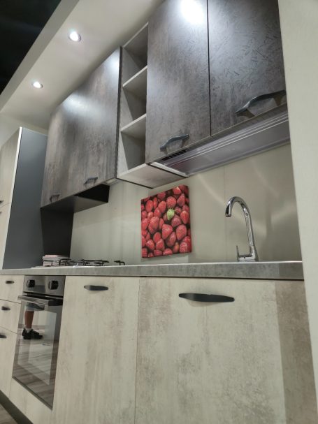 Moderne keuken met grauwe kasten, roestvrijstalen werkblad en een kleurrijk fruitafdruk.