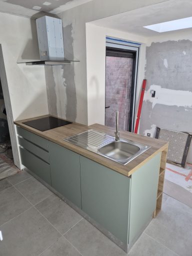 Moderne keuken met een groen meubel en een dubbele spoelbak op een houten blad.