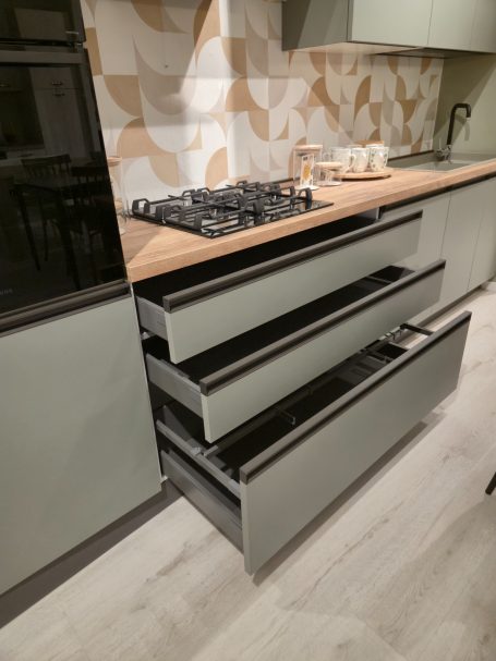 Moderne matgroene keuken Drie open lades onder een moderne kookplaat in een lichtgroene keuken.