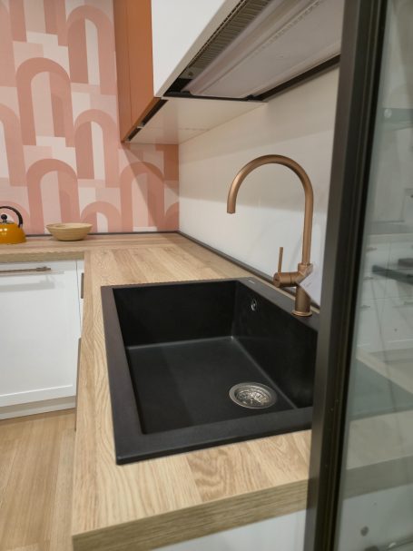 Composiet Moderne keuken met een zwart spoelbak en een koperkleurige kraan op een houten werkblad.