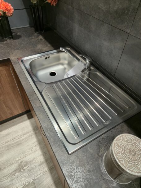 Warme uitstraling, slim ontworpen Een roestvrijstalen spoelbak met een kraan, geplaatst op een moderne aanrecht.
