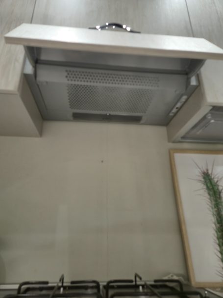 Staal kleurige afzuigkap boven een kookplaat in een moderne keuken.