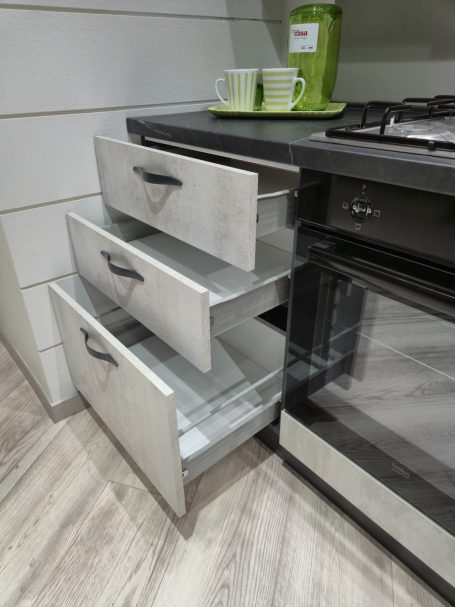 Mira keuken – Moderne rechte keuken met houtlook Keuken met open lades onder een kookplaat en twee groene mokken bovenop.