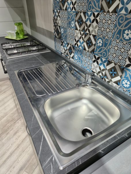Mira keuken – Moderne rechte keuken met houtlook Rvs spoelbak met een moderne tegelfonds in een keuken.