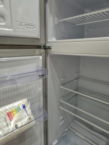 Lege koelkast met één lade en schappen, zichtbaar plastic verpakking aan de linkerkant.