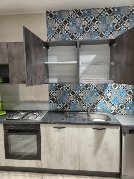 Mira keuken – Moderne rechte keuken met houtlook Moderne keuken met open bovenkasten en kleurrijke betegeling op de muur.