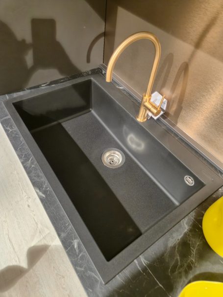 Moderne antracietgrijze keuken Diepe zwarte spoelbak met een gouden kraan en een afvoer.