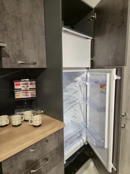 Een open koelkast met een houten aanrecht en enkele mokken ervoor.