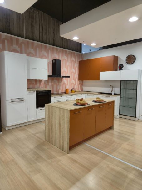 Een hoekkeuken naar uw wensen Moderne keuken met een eiland, witte en houten kasten en roze wanddecoratie.