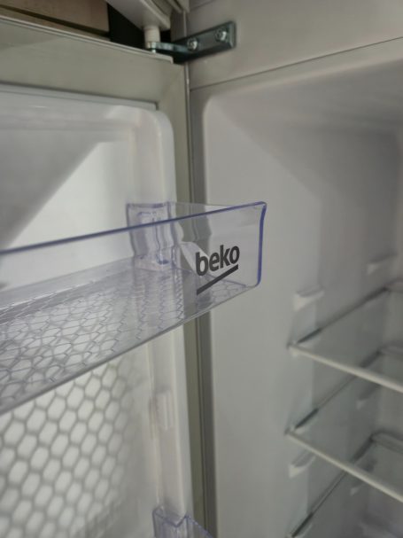 Transparante plastic lade met "Beko" logo in een open koelkast.