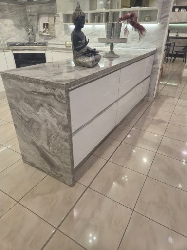 Moderne keuken met marmeren eiland en witte lades, verlicht door binnenverlichting.