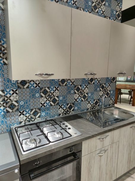 Moderne keuken met een inox aanrecht, fornuis en kleurrijke betegeling aan de muur.