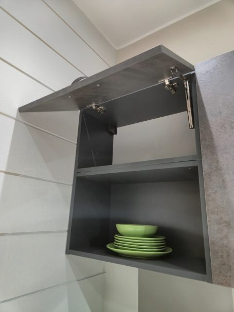 Mira keuken – Moderne rechte keuken met houtlook Zwart keukenkastje met een open deur en groene borden op de plank.