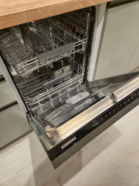 Moderne matgroene keuken Een open vaatwasser met een houten blad en metalen rekken.