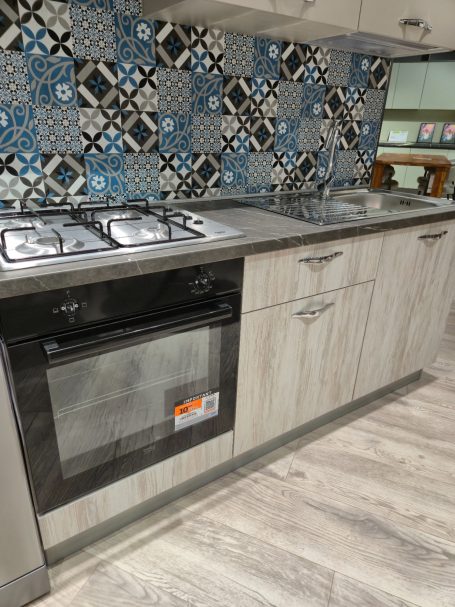 Moderne keuken met een gasfornuis en een betegelde wand in blauw en grijs.
