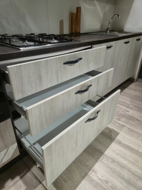 Drie open lades van een moderne keuken met een kookplaat ernaast.