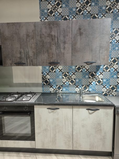 Mira keuken – Moderne rechte keuken met houtlook Moderne keukenkasten met blauwe en zwarte tegels op de achtergrond.