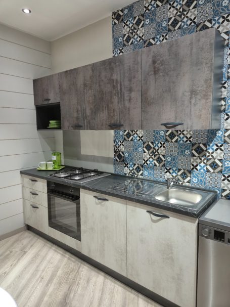 Mira keuken – Moderne rechte keuken met houtlook Moderne keuken met grijze kasten, blauw mozaïek achterwand en RVS apparatuur.